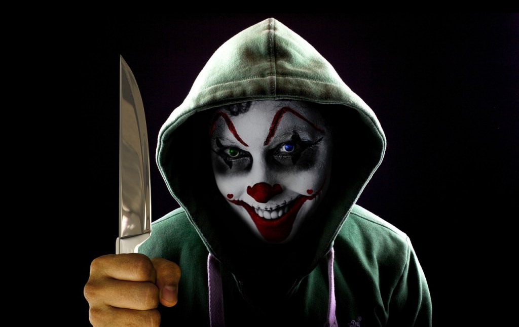 A portrait of a clown wearing a hoody and holding a big knife